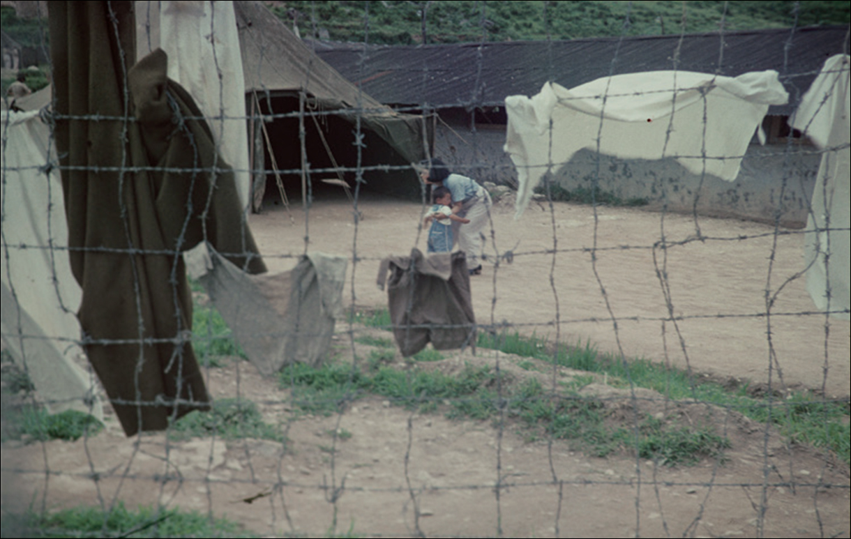 ▲ 수용소의 아이와 엄마(거제 포로수용소에 수용된 포로 중에 아이와 여성이 있었다. 이중 철망 안으로 기저귀로 보이는 빨래와 아이, 그리고 어머니의 모습이 보인다.) (1952. 7. 18, NARA 소장)<br>